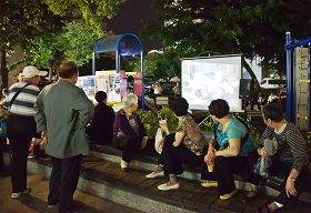 大陸遊客逛高雄六合夜市，累了歇一會兒，剛好來看看展板、電視，了解法輪功真相。