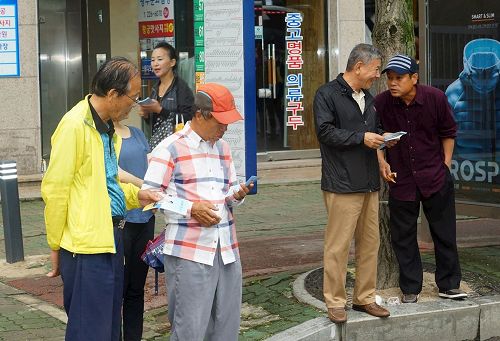 '圖4：兩旁的民眾接過法輪功學員分發的真相資料後，馬上閱讀。'