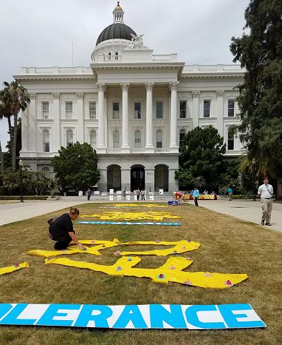 '圖10：此次活動，法輪功學員們帶著自己做的蓮花給每個議員辦公室送一朵蓮花，邀請他們的工作人員到活動現場，把蓮花放到擺在草坪上的「真、善、忍」三個大字上。有好多位議員辦公室的工作人員，拿著蓮花下樓到草坪上，把花擺到「真、善、忍」的字上。他們並與法輪功學員攀談了解更多講真相，還拿了法輪功簡介，表示要進一步了解法輪功，並且感謝法輪功學員來這裏告訴他們法輪功。'