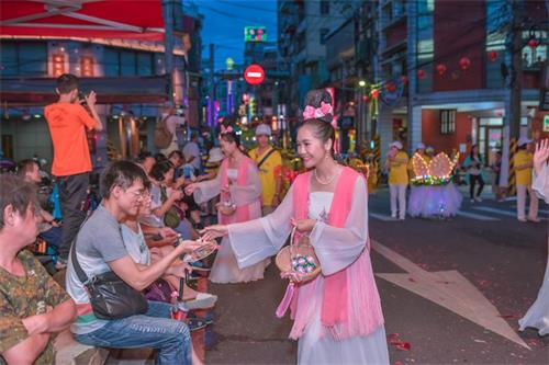 '圖3：青年法輪功學員裝扮的仙女隊向兩旁觀眾發放蓮花'