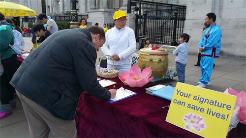 圖4～5：在倫敦特拉法加廣場北台階，民眾為「世界法輪大法日」慶祝活動所吸引，駐足了解真相，他們在明白真相後紛紛簽名支持法輪功反迫害。