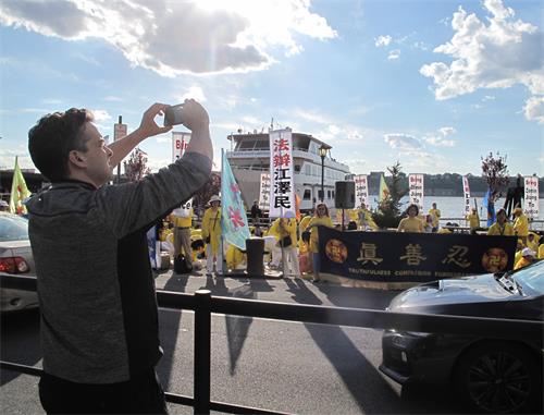 一位在金融部門工作的紐約人被法輪功學員的和平抗議場面所吸引，他拿出手機認真錄下眼前看到的壯觀場面，表示要發給自己的朋友去看。