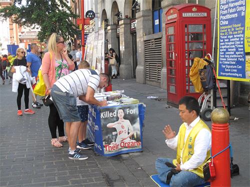 '圖2：在倫敦唐人街，「反迫害二十週年」遊行隊伍讓一對英國夫婦第一次看到法輪功真相，他們馬上來到法輪功學員在唐人街講真相點繼續了解真相，並簽名支持制止迫害。'