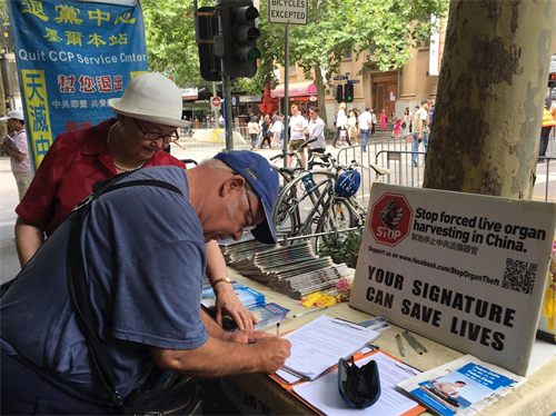 '圖13：在吉朗市一所學校工作的布萊爾（Richard Blair）觀賞遊行後，在唐人街的真相點簽名，要求澳洲政府幫助制止中共的反人類罪行，希望中國民眾最終能享有自由。'