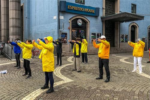 '圖1：法輪功學員在音樂廳旁舉辦講真相活動。學員們在雨中展示功法。'