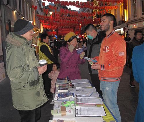 '圖8：二零二零年二月一日，在倫敦唐人街，法輪功學員把«九評共產黨»一書和«共產主義的終極目的»報紙送給一位在英國攻讀政治學學位的台灣留學生（戴口罩者）。'