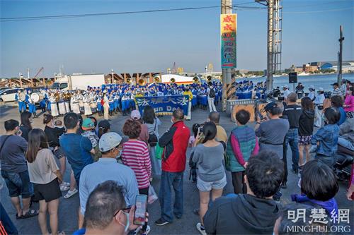 '圖2：傍晚，法輪功天國樂團受邀轉往興達港觀光漁市演出，樂音響徹天空。天色雖晚，仍不減民眾的熱情圍觀，觀眾紛紛拿出手機拍攝，並報以掌聲和歡呼聲。'