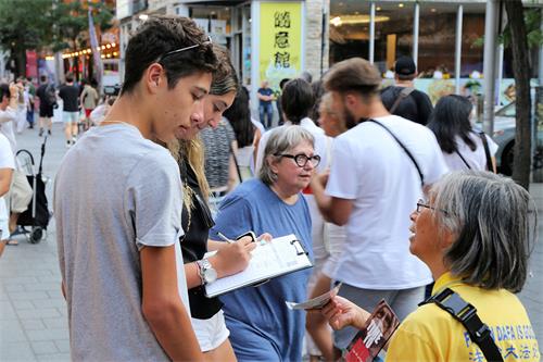 圖7:二零二二年七月十九日，魁北克部份法輪功學員在蒙特利爾唐人街舉行燭光夜悼。圖為現在民眾在制止迫害請願書上簽字。